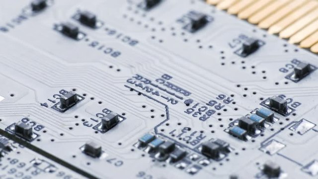 Rotating white printed circuit board, microprocessors, capacitors and audio connectors, partially covered with electrostatic dust.
