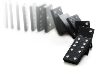 Domino effect with falling black dominoes on a white background, selective focus and very narrow...
