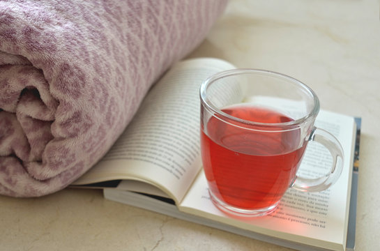 Cup of red tea over some books and a blanket in the background