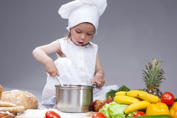 Portrait of Caucasian Little Girl In Cook Uniform Working With Scoop and Saucepan In Studio.Posing Against Gray Background