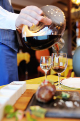 the waiter pours red wine from a beautiful bottle against the background of the restaurant and food