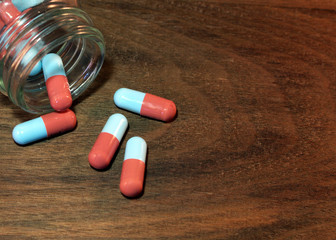 Prescription drug abuse concept. Blue and red capsules spilled onto a dark wooden  table from a glass bottle. 