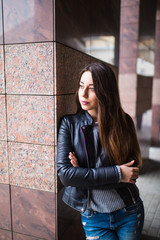 Beautiful young girl in a stylish jacket near buildings on the street