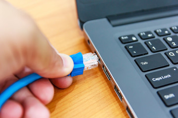 Human hand plugging in a LAN cords into the personal laptop computer, Selective focus