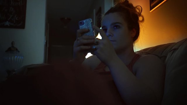 A Millennial woman is engrossed in a tv show in her living room at night