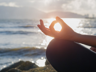 Yoga concept. Closeup woman hand practicing lotus pose on the beach at sunset