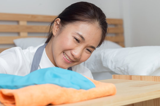 Happy Asian maid cleaning dust on table with glove and microfiber