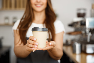 Coffee Business Concept - Beautiful Caucasian lady smiling at camera offers disposable take away hot coffee at the modern coffee shop