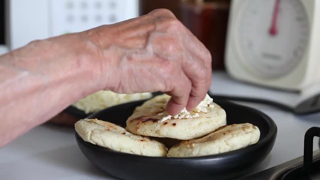 Hands of a senior woman adding shredded cheese to a roasted arepa