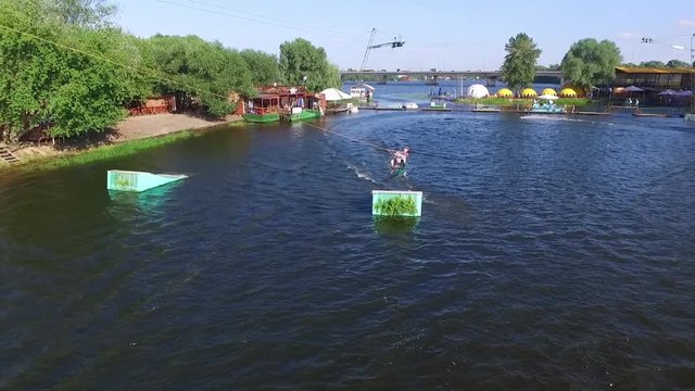 Flying over wakeboarding cable wake park HD aerial video. Wakeboarder doing jump tricks and crash. Water extreme sport.