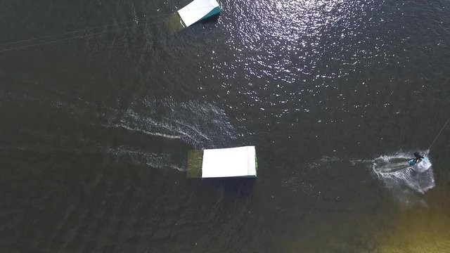Flying over wakeboarding cable wake park HD aerial video. Wakeboarder doing tricks: jump flip somersault. Water extreme sport.