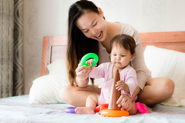 Happy mother teaches 2 year old daughter coordination skills using plastic hoop toys