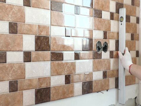 he worker's hands are using construction level to align the ceramic tile on the wall.