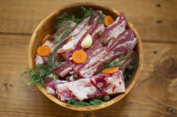 Fototapeta na wymiar Pork meat with vegetables. Raw pork ribs prepared for cooking. Carrot and garlic with fat in Clay bowl