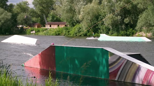 Wakeboarder doing tricks at cable wake park HD wakeboarding slow-motion video. Water extreme sport. Man jumps and rotates