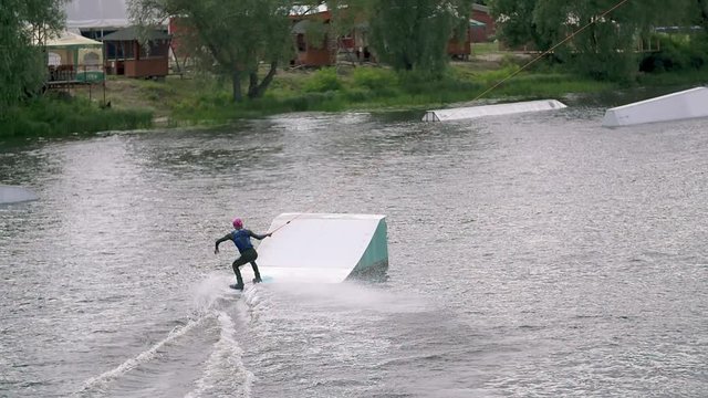 Wakeboarder doing tricks at cable wake park HD wakeboarding slow-motion video. Water extreme sport. Man jumps and crashes