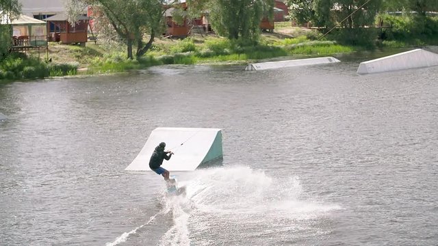 Wakeboarder doing tricks at cable wake park HD wakeboarding slow-motion video. Water extreme sport. Man jumps and crashes