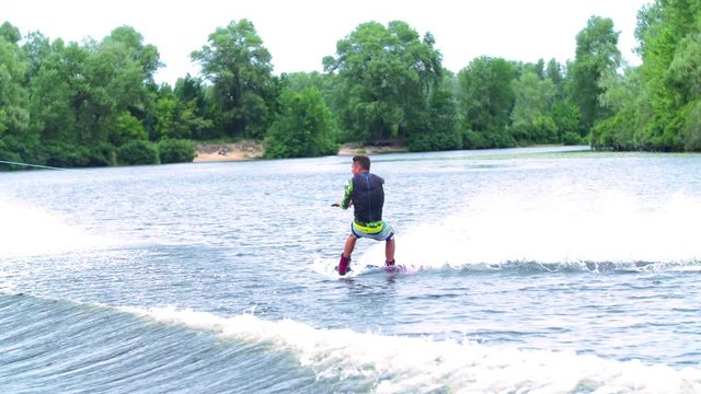 Wakeboarder doing tricks HD wakeboarding slow-motion video. Man rides behind boat and jumps somersault flip on waves. Water extreme sport.