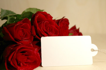 A bouquet of dark red roses with a white blank label on a wooden background