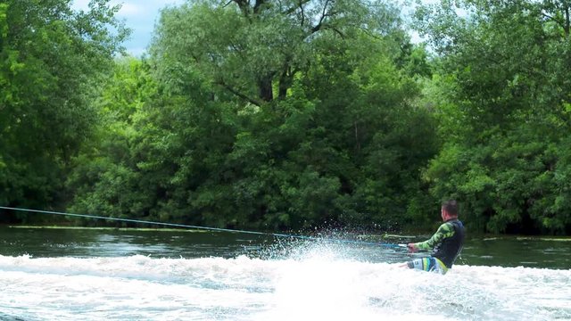 Wakeboarder doing tricks HD wakeboarding slow-motion video. Man rides behind boat and jumps somersault flip on waves. Water extreme sport.