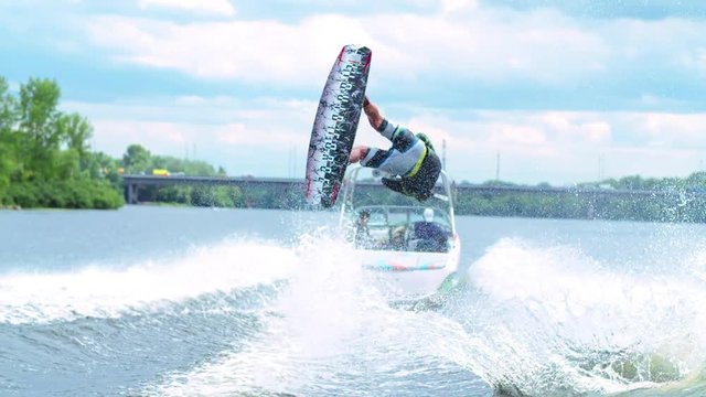 Wakeboarder doing tricks HD wakeboarding slow-motion video. Man rides behind boat and jumps somersault flip on waves. Water extreme sport.
