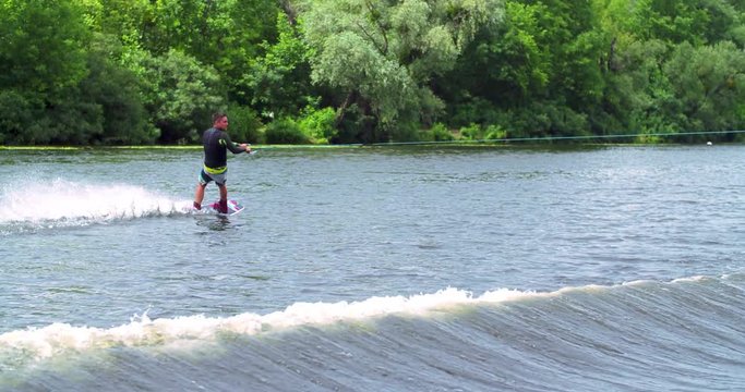 Wakeboarder doing tricks 4k wakeboarding video. Man rides behind boat and jumps somersault flip on waves. Water extreme sport.