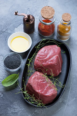 Metal plate with raw fresh medallion beef steaks and seasonings, selective focus, vertical shot