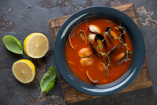 Top view of tomato soup with vongole clams and mussels served in a dark gray plate on a brown stone background