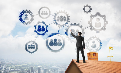 Businessman on house roof presenting teamwork and connection concept. Mixed media