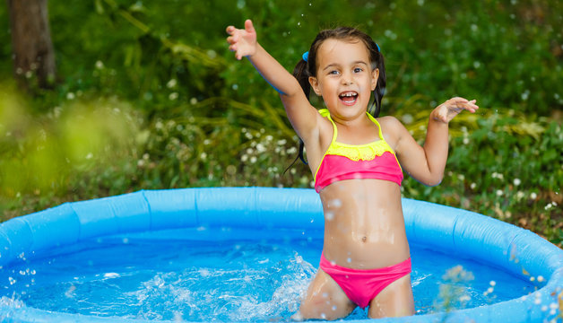 Little girl in an inflatable pool in the garden near the house - Powered by Adobe