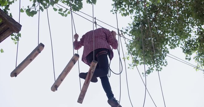 Male teenager moving on adventure rope park 4k video. Young climber walk on rope ladder board for extreme adventure