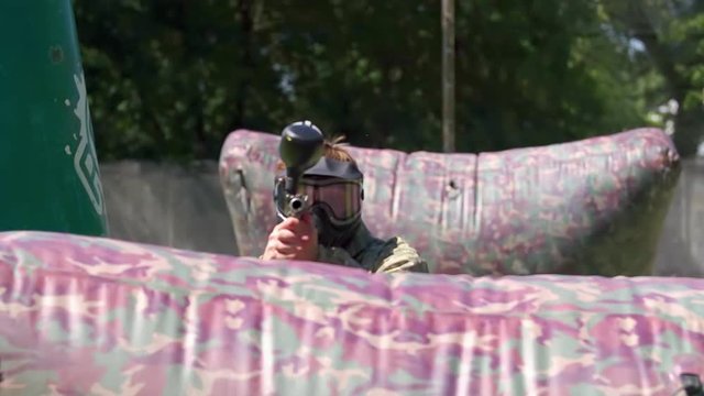 Paintball player aiming and shooting target HD game slow-motion POV video. Man with gun hitting to camera on playing field. Ball flying and painting camera