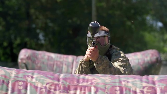 Paintball player aiming and shooting target HD game slow-motion POV video. Man with gun hitting to camera on playing field. Ball flying and painting camera