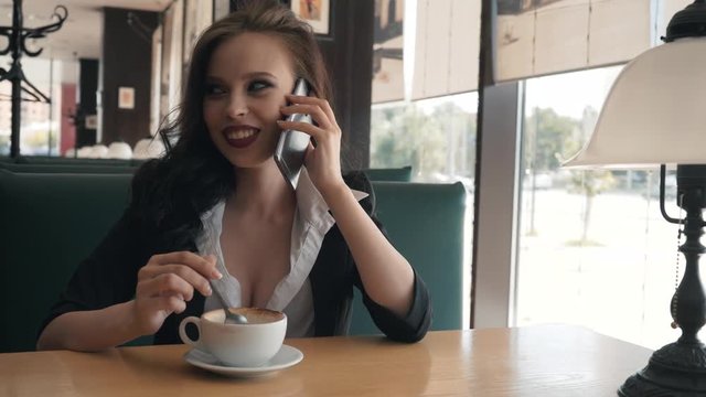 Young beautiful modern woman speaks with a girlfriend on the phone. A girl is resting in a cafe, talking on the phone.