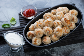 Frying pan with roasted meat dumplings or pelmeni on a black wooden serving board, horizontal shot