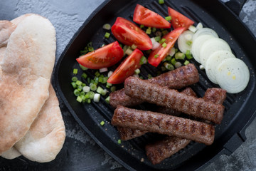 Top view of grilled cevapcici or skinless beef sausages with pita bread, onion and tomatoes, close-up