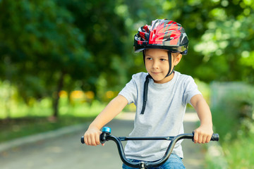 Obraz premium Little boy learns to ride a bike in the Park near the home. Portrait of a cute kid on bicycle. Happy smiling child in helmet riding a cycling.