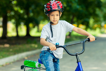 Obraz premium Little boy learns to ride a bike in the Park near the home. Portrait of a cute kid on bicycle. Happy smiling child in helmet riding a cycling.