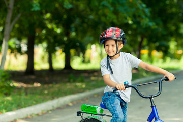 Little boy learns to ride a bike in the Park near the home. Portrait of a cute kid on bicycle. Happy smiling child in helmet riding a cycling.