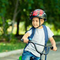 Fototapeta na wymiar Little boy learns to ride a bike in the Park near the home. Portrait of a cute kid on bicycle. Happy smiling child in helmet riding a cycling.