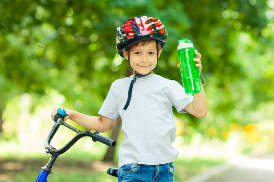 Little boy drinking water by the bike. Happy smiling child in helmet riding a cycling.