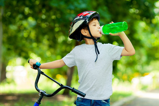 Little boy drinking water by the bike. Child in helmet riding a cycling.