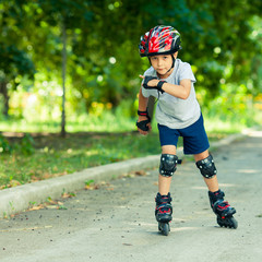 Little boy riding on rollers in the summer in the Park. Happy child in helmet learning to skate.