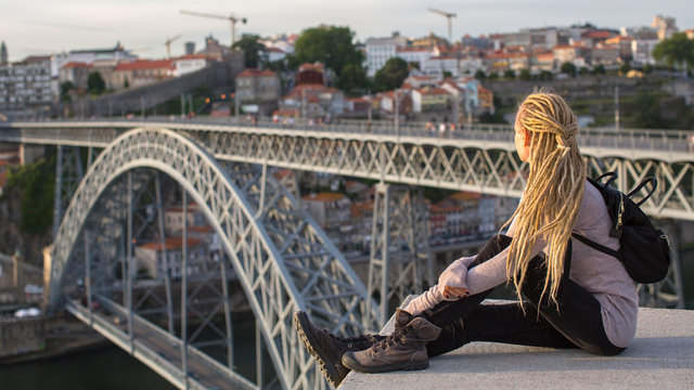 Young female sitting on the top observation deck on the Douro river, overlooking the bridge Dom Luis I, Porto, Portugal.