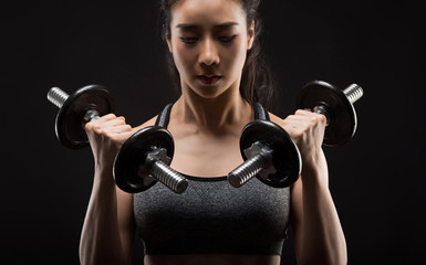 Beautiful girl exercising squatting with dumbbells on black.