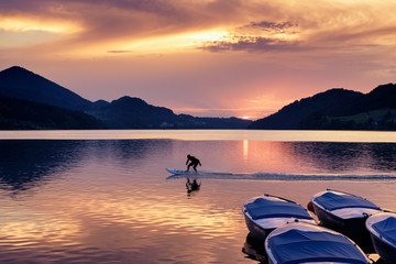 Sunset at Lake Fuschl with silhouette of a man riding an electric surfboard, boats in foreground, Fuschl am See, Fuschlsee, Salzburg state, Salzkammergut, Austria, Europe