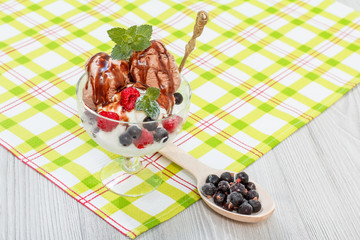 Chocolate and white ice cream in a glass with raspberry and currant berries and mint leaves on checkered napkin