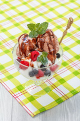Chocolate and white ice cream in a glass with raspberry and currant berries and mint leaves on checkered napkin
