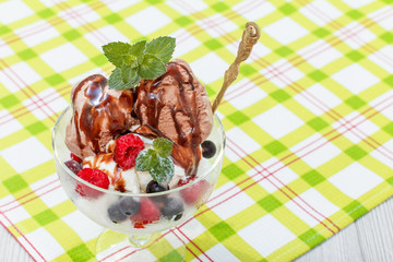 Chocolate and white ice cream in a glass with raspberry and currant berries and mint leaves on checkered napkin