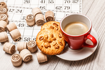 Board game lotto on white desk. Wooden lotto barrels and game cards with cup of coffee and cookies on plate